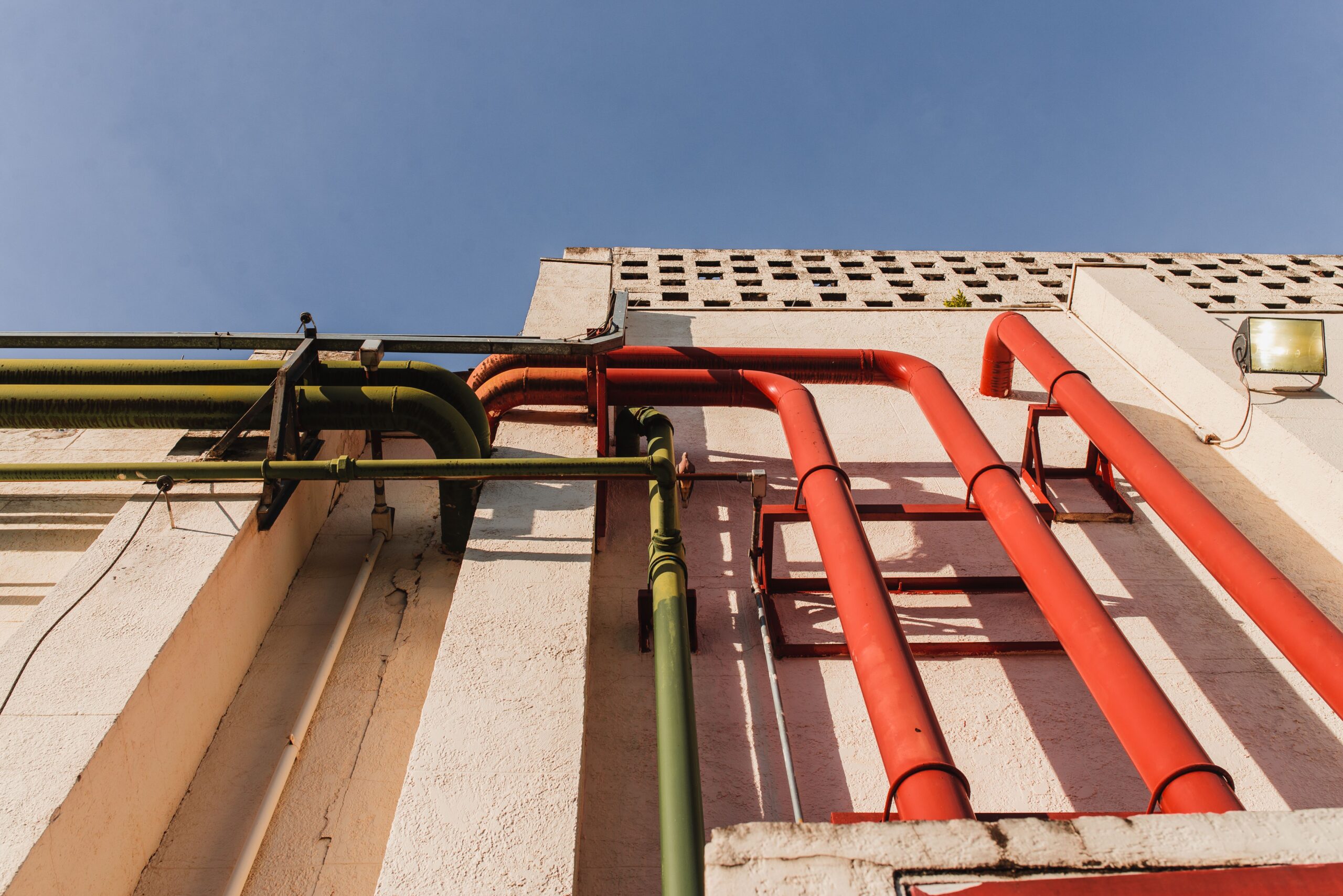 Ged and green plastic pipes on a sunlit exterior building wall